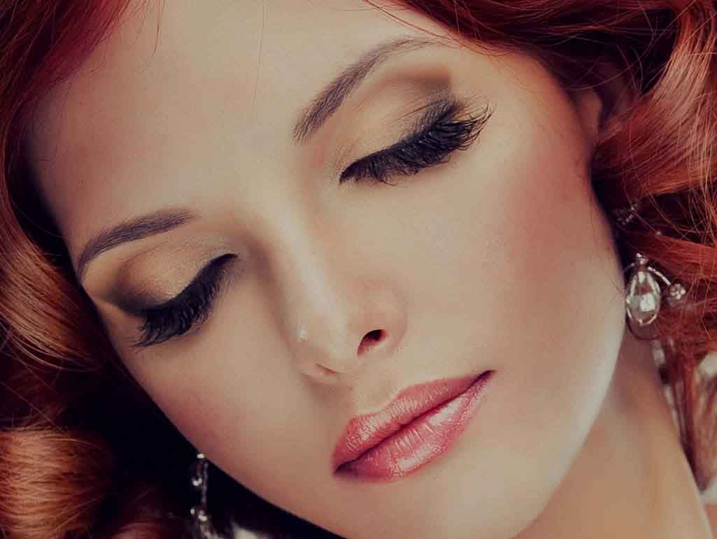 Rostro de una mujer con  ojos cerrados maquillados en color café, pestañas largas y labios rosados